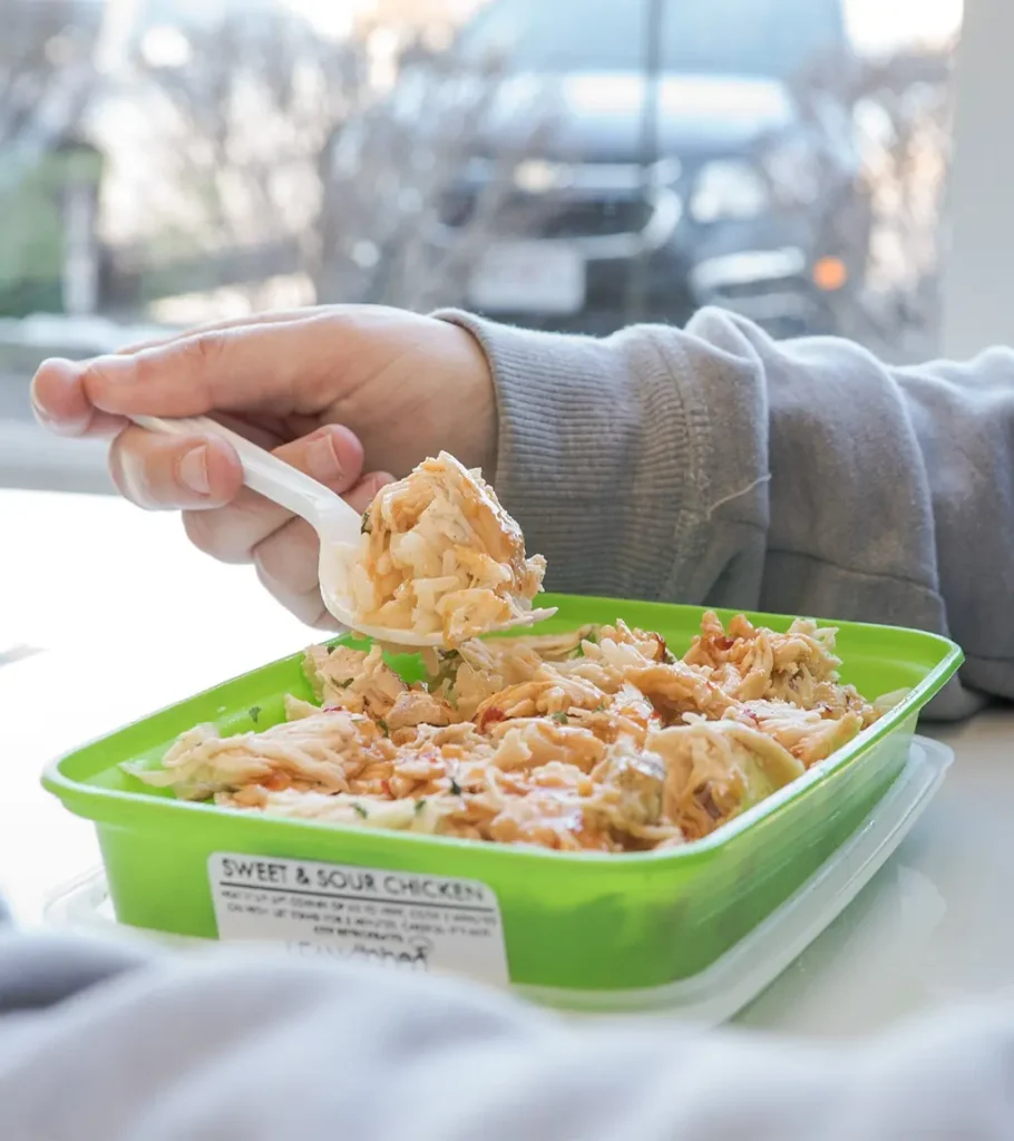 Person eating sweet and sour chicken from a green Lean Kitchen meal prep container