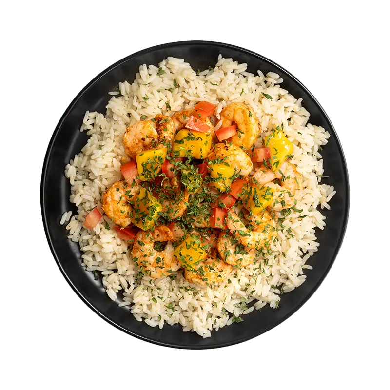 Coastal Mango Shrimp with seasoned shrimp, rice, mango, diced tomatoes, and herbs in a black bowl